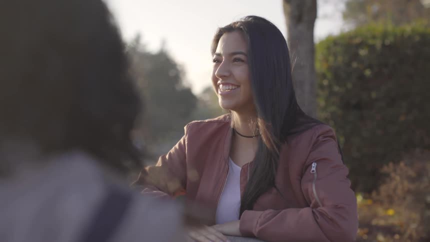 A hispanic woman laughs and smiles while talking to friends