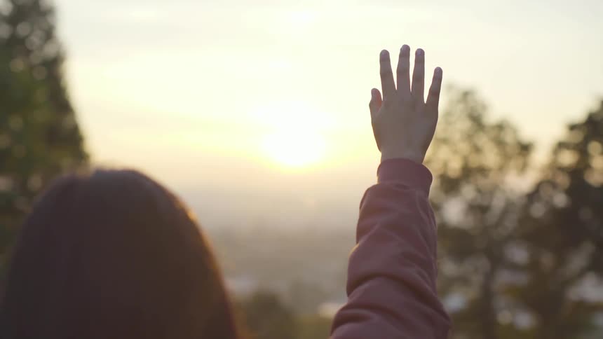 A woman reaches into the air outside at sunset