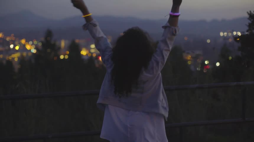 A woman waves glow sticks at a city overlook