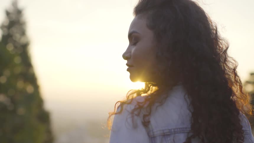 A woman standing outdoors with her eyes closed in the evening