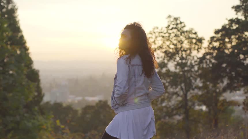 A hispanic woman stands outdoors and looks off into the distance