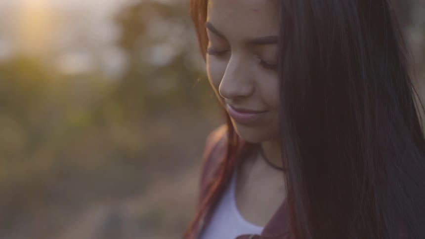 A hispanic woman standing outdoors with her eyes closed at sunset