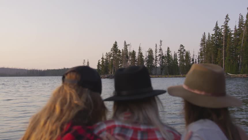 Three girl friends side by side wearing hats and looking out at the lake