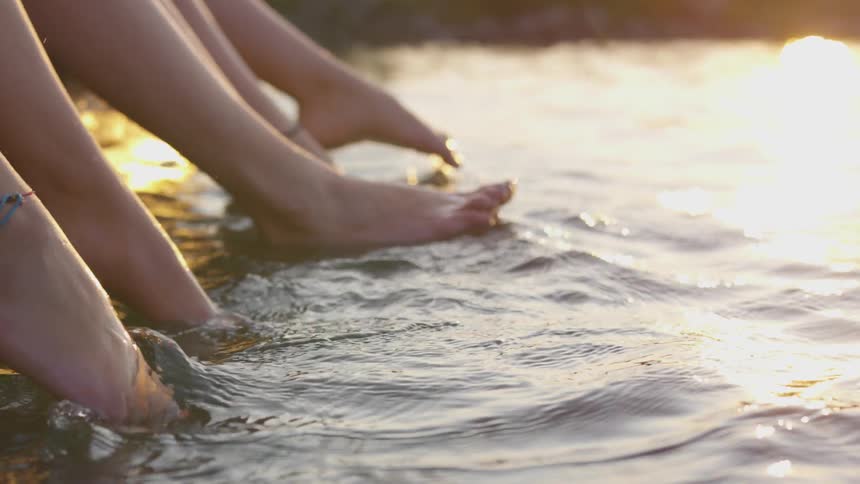 The feet of three girl friends kick and splash at the waters surface at sunset