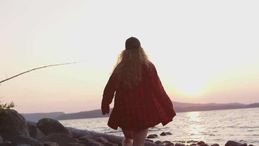 A woman walks down the rocky shore of a lake
