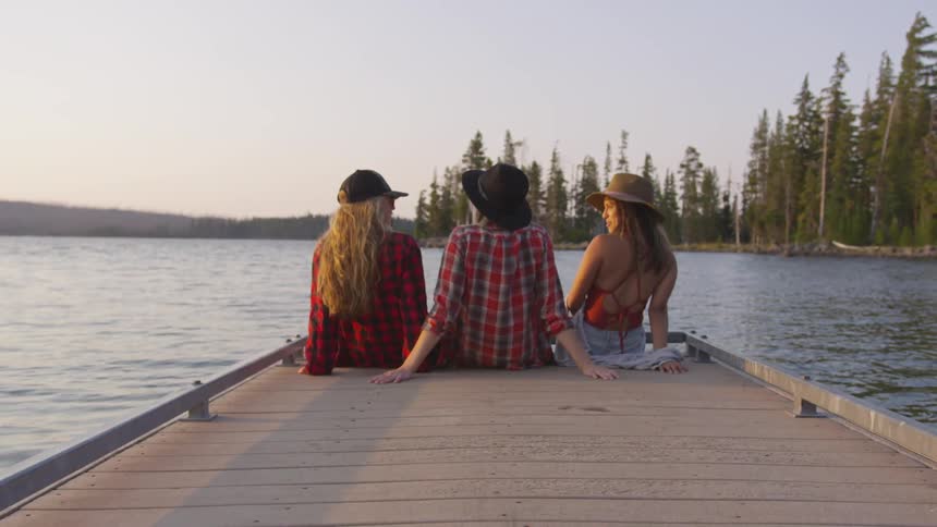 Three women sit on a dock on a lake