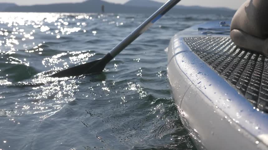 A person paddles while kneeling on a paddle board