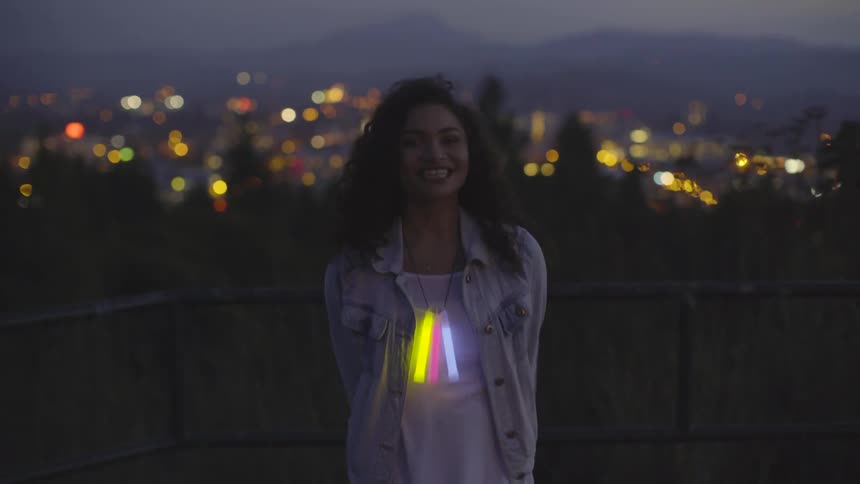 A woman waving colored glow sticks around at dusk