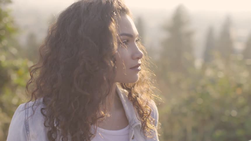 A woman standing outside with the sun in her face and trees in the background