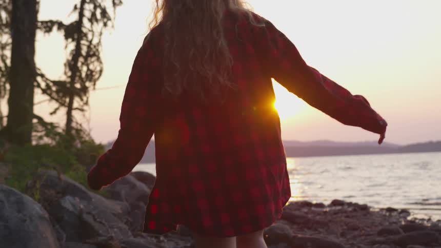 A woman walks down a rocky beach next to a lake