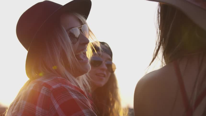 Three women with hats outside talking with the sun in the background