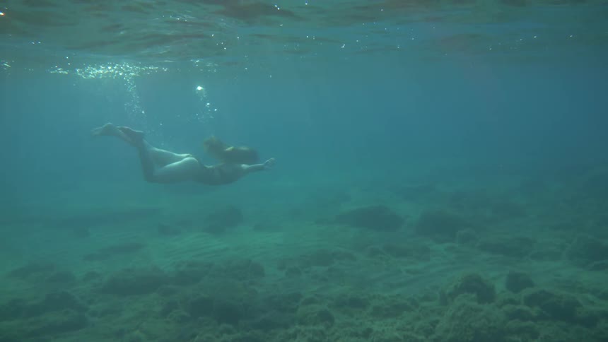 A woman swims through the water and comes up to the surface