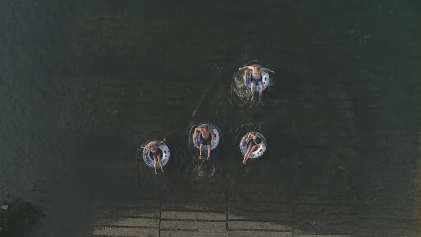 Four people enter a lake and float on round tubes