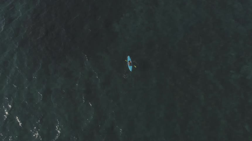 A person paddles a pale blue kayak on the water on a sunny day