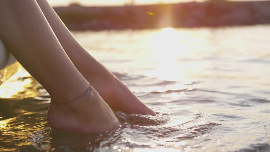 Three people sit and paddle their feet in water at sunset