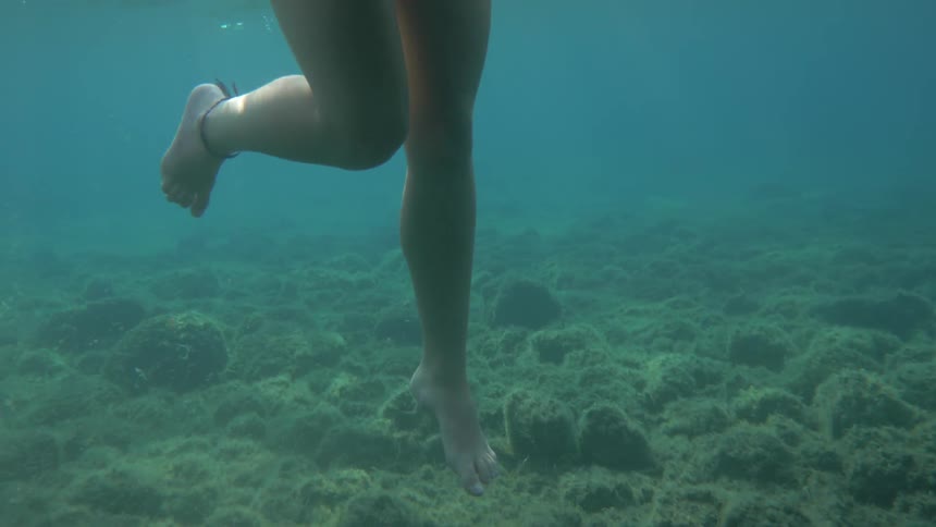 A womans legs kick underwater while swimming in an ocean