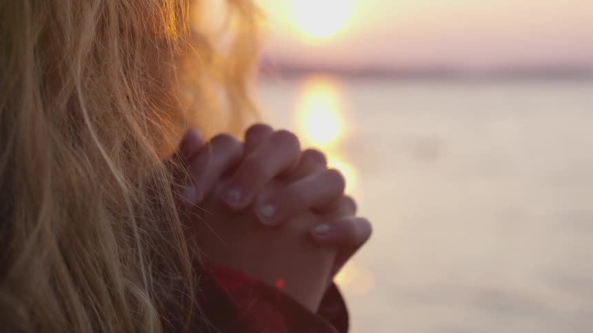 A woman clasps her hands next to a body of water