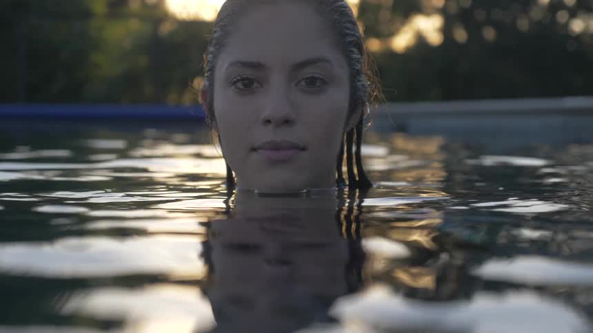 A woman stands in pool water up to her neck at sunset