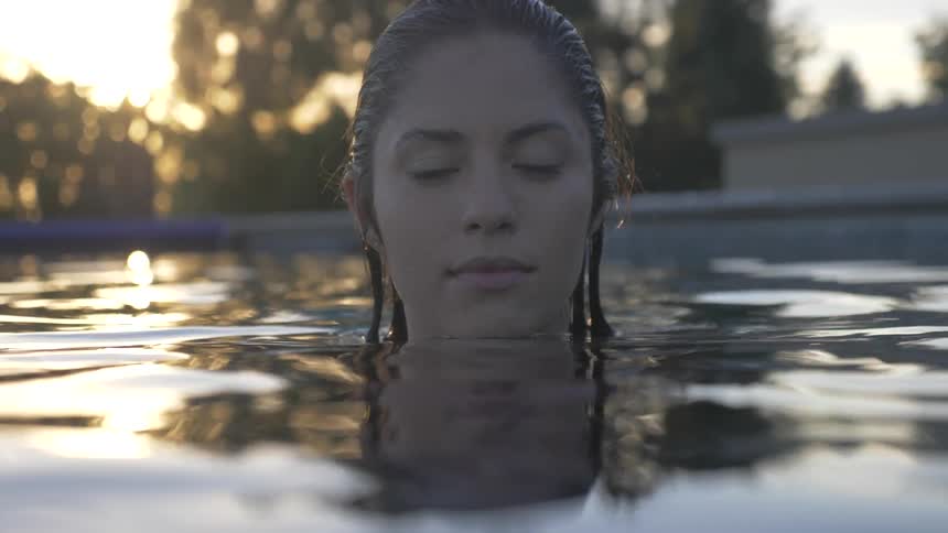A woman stands in a pool with the water up to her neck at sunset