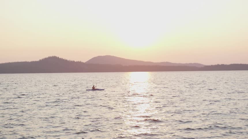 A person rides in a kayak on a mountain lake at sunset