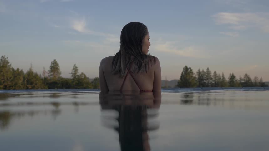 A woman stands waist deep in water and looks around at the trees and sky