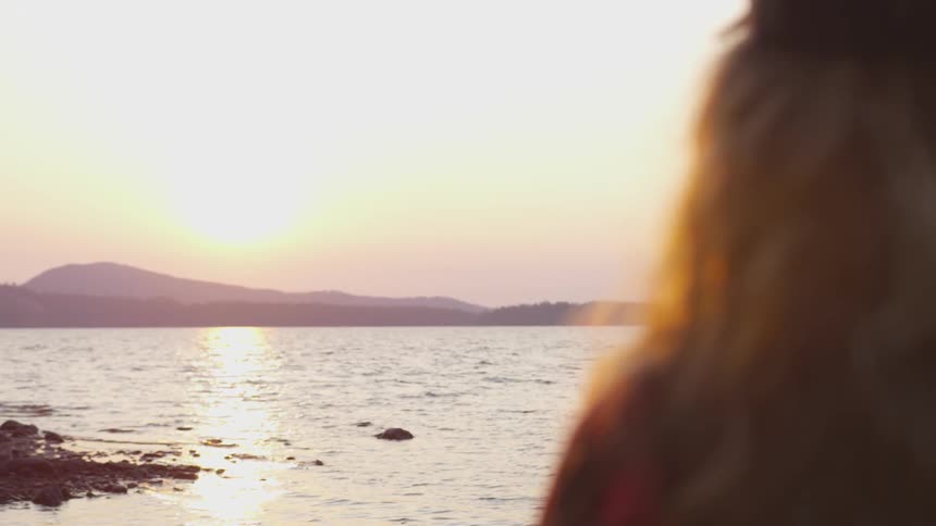 A woman outside standing staring at a lake