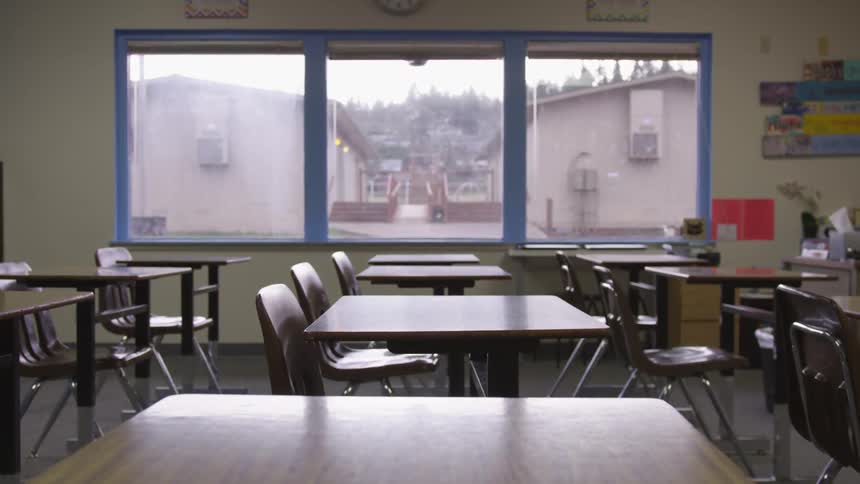 Empty desks sit near a window in a school classroom