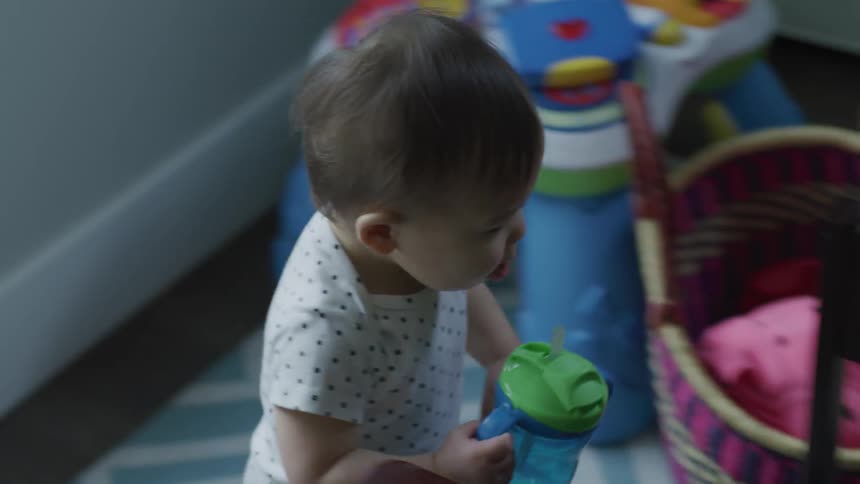 A toddler carries a sippy cup across a rug