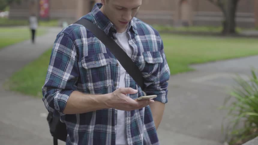 A young white man fiddles with a smartphone