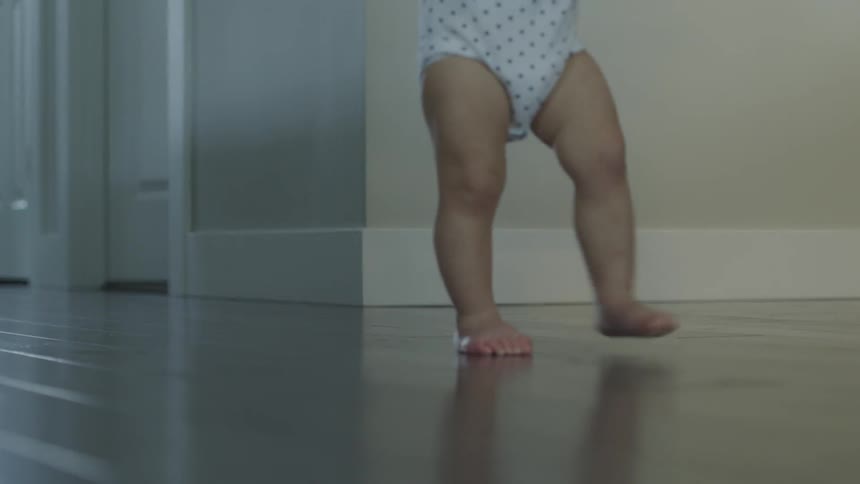 A toddler walks across a wood floor
