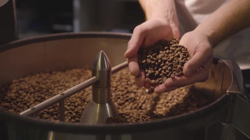 A man is holding coffee beans by a machine
