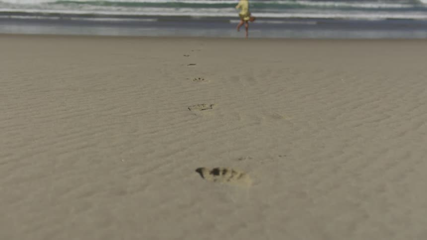 A blonde woman runs on the sand leaving foot prints to the ocean