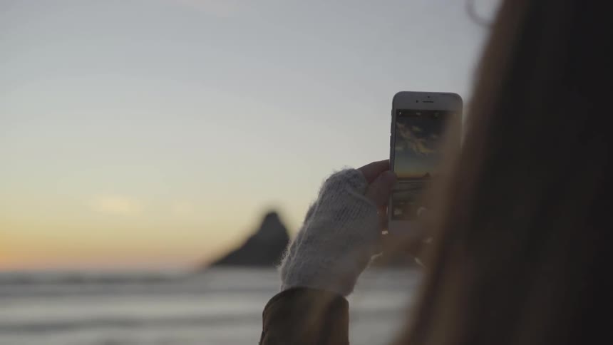 A woman takes a picture of the ocean