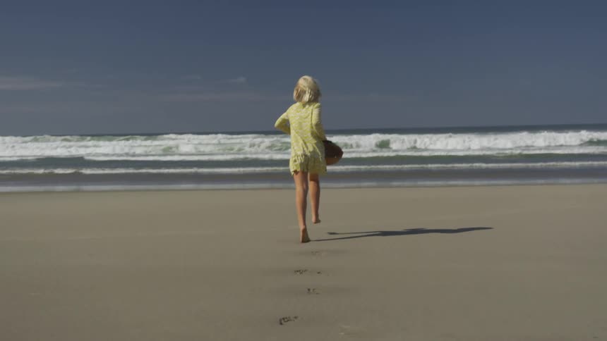 A blonde girl runs on a sandy beach barefoot while carrying a basket