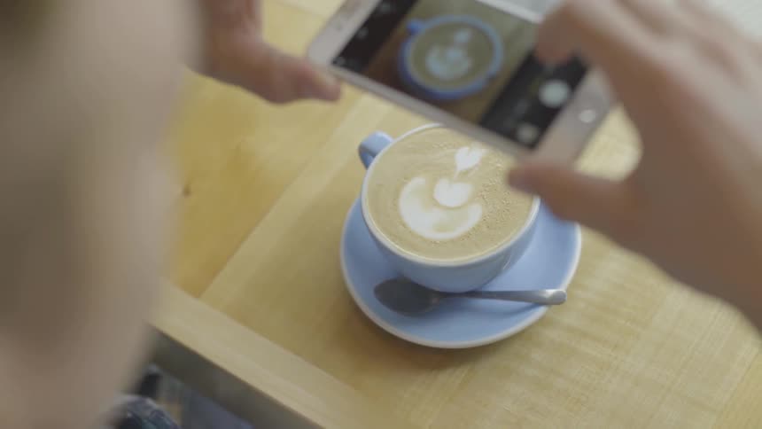 A person takes a picture of a latte with their smartphone