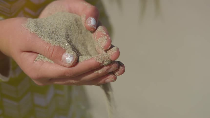 Sand sifts through a girls hands on a beach