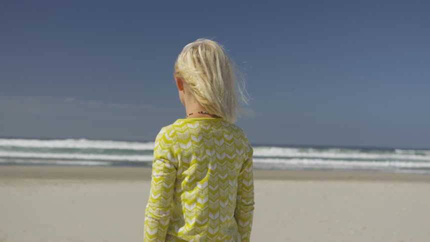 Woman stands on beach looking out to sea