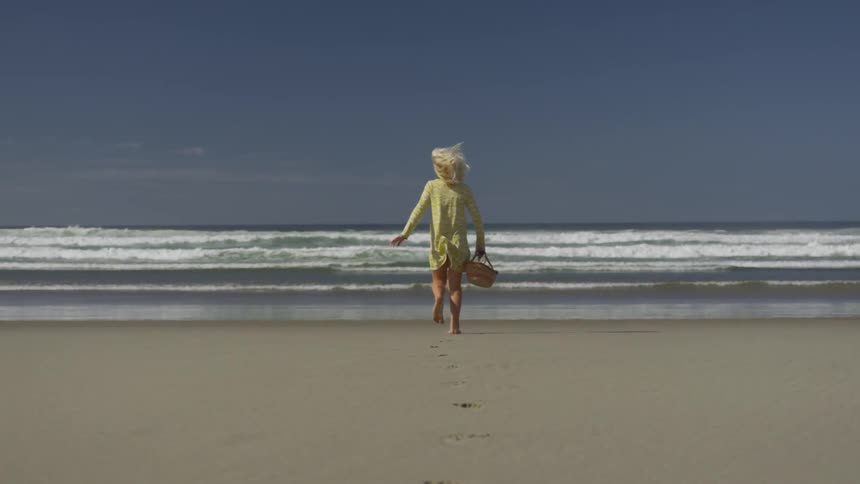 A blonde girl runs on a sandy beach while holding a basket