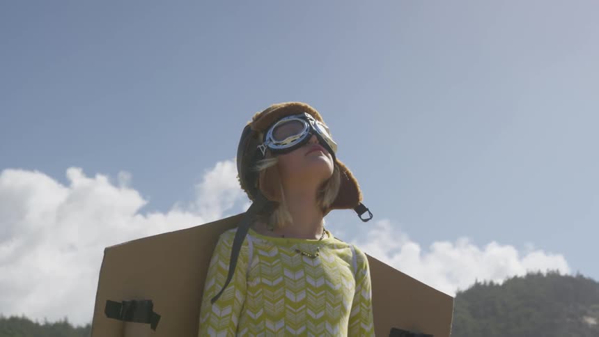 Child wears goggles an aviator cap and cardboard backpack