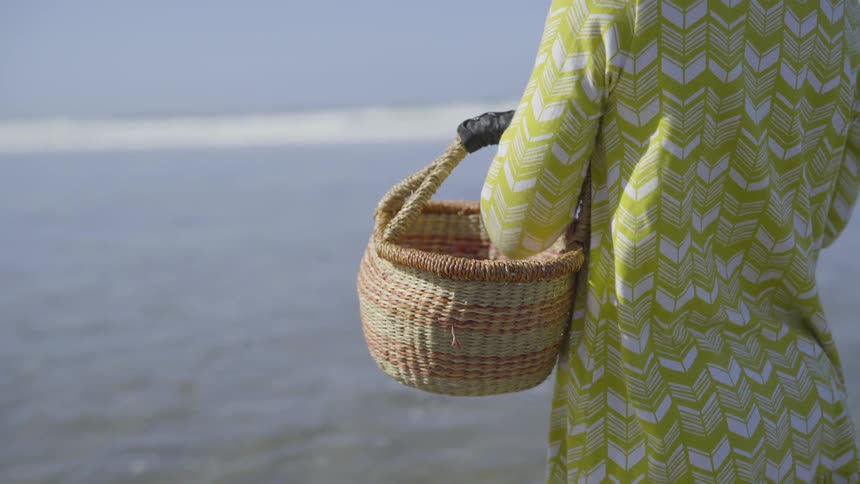A young girl with a basket sands on the beach