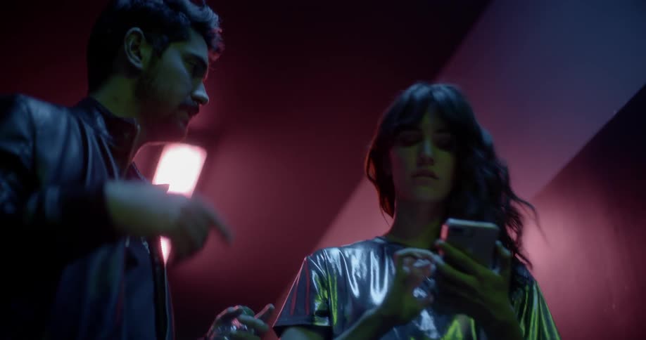 A woman fiddles with a smartphone as a man walks up and tells her to move along
