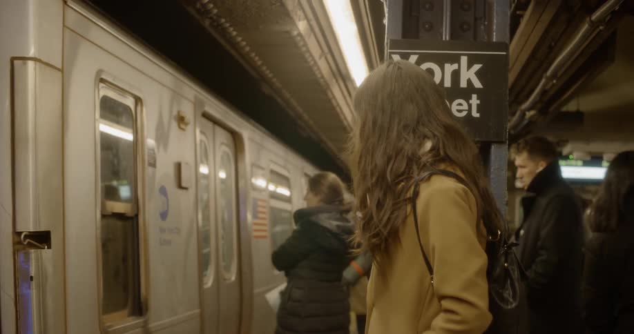 A woman in a subway train station picks up her bags then walks towards the train