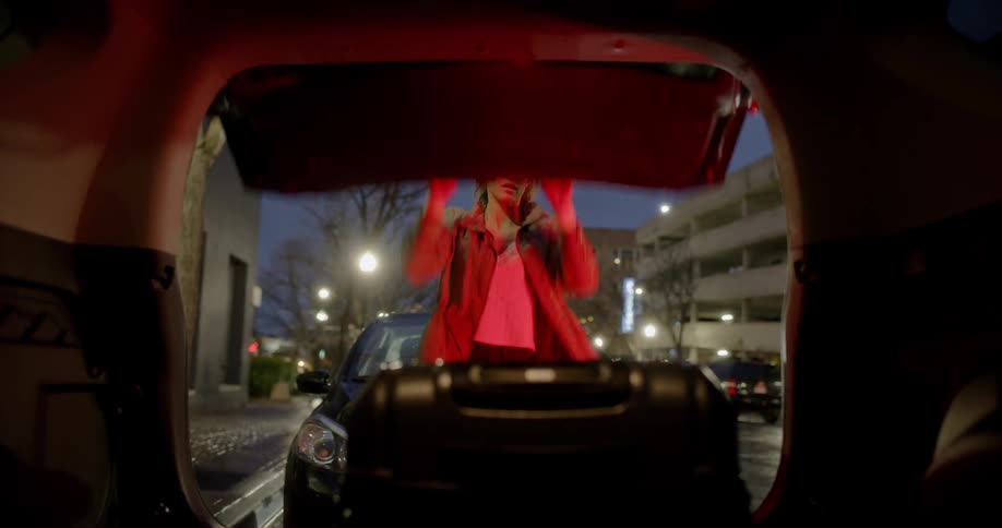 A woman puts a suitcase in the back of a car