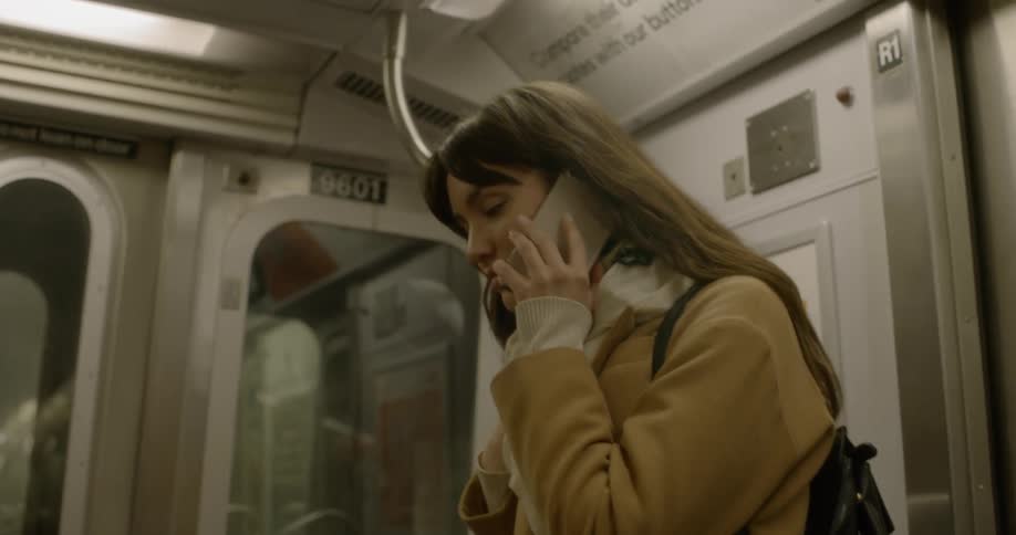 A woman in a mustard colored coat is on the phone on the subway