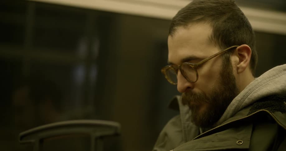 Man sighs and takes off his hat while riding train