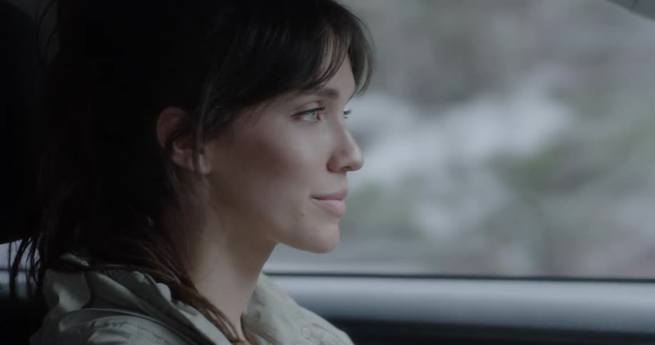 A woman smiles while driving a car in a snowy environment