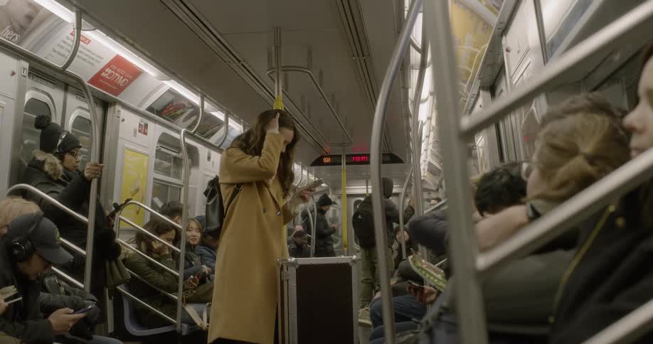 A woman wearing a coat looks at her smartphone on a subway car