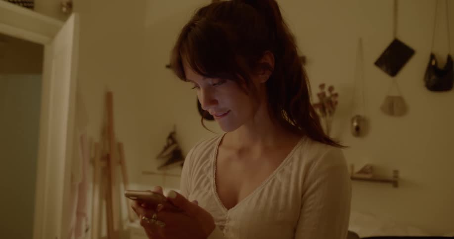 A white woman picks up a smartphone and looks at it