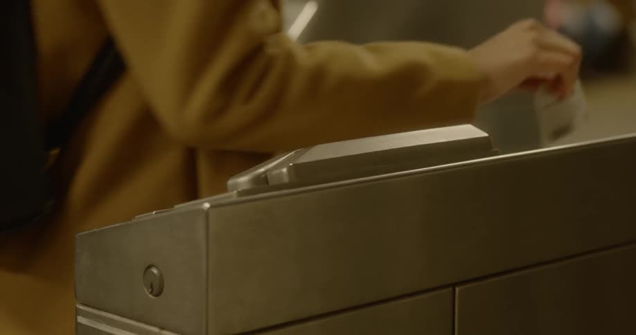 A woman in a mustard colored coat swipes her ticket for the subway
