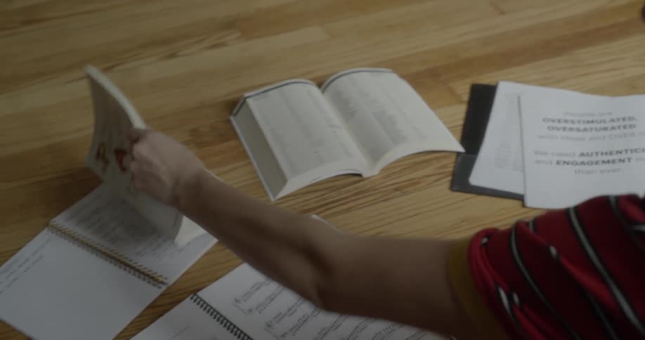 A young woman writes in a notebook and then flips through a book